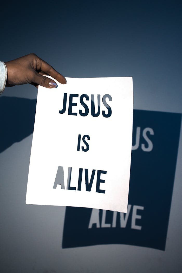 A person holding a white paper with the message 'Jesus is Alive' against a blue background.